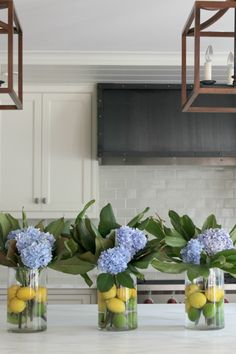 four vases filled with flowers and lemons on top of a kitchen countertop