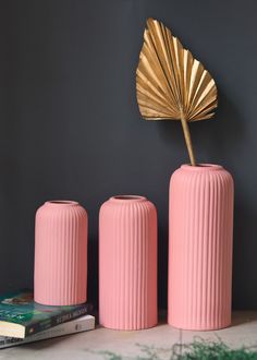 three pink vases sitting on top of a table next to books and a gold fan