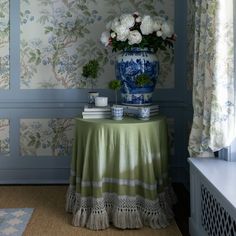 a blue and white vase sitting on top of a table next to a wall with flowers