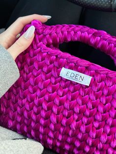 a hand holding a pink woven bag with a name tag on the front and side