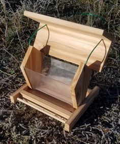 a wooden bird feeder sitting in the grass