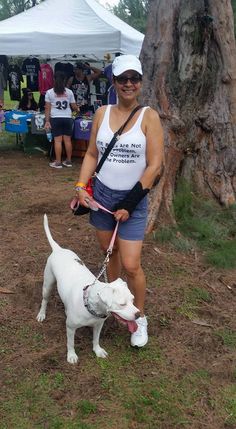 a woman in white tank top and blue shorts with dog on leash at outdoor event