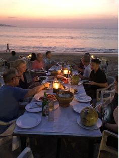 a group of people sitting at a table with food and drinks on it near the ocean