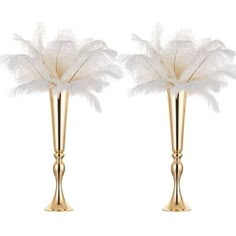 two tall gold vases with white feathers in them on a white background for decoration