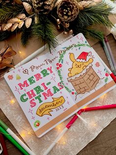 a christmas greeting card with pine cones and pencils on the table next to it