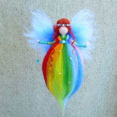 a rainbow colored doll with wings and beads on it's head is hanging from a wall