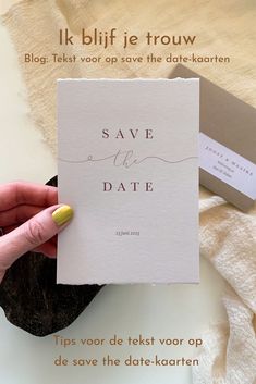 a person holding up a save the date card on top of a table with other items