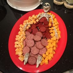 a red plate topped with sausages, cheese and other food items on top of a black counter