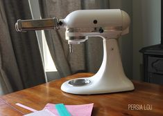 a white mixer sitting on top of a wooden table next to a pair of scissors