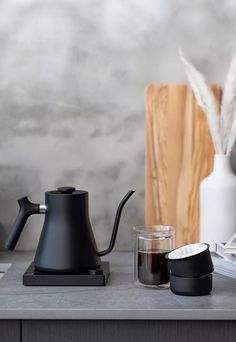 a black coffee pot sitting on top of a counter next to a cup and saucer