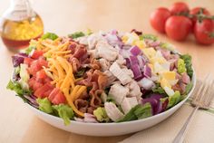 a salad with chicken, lettuce, tomatoes and cheese on it next to a fork