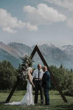 a bride and groom standing in front of a wooden structure with mountains in the background