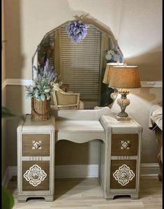 a white vanity with two drawers and a mirror on it's side, next to a lamp