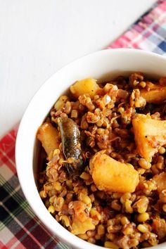 a white bowl filled with food sitting on top of a checkered table cloth next to a spoon