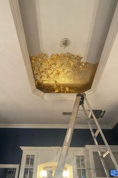 a ladder that is in front of a ceiling with gold paint on it and some windows