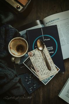 a cup of coffee sitting on top of a table next to books and a spoon