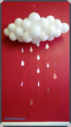 white balloons are suspended from the ceiling in front of a red wall with raindrops