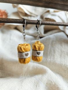 two small knitted objects hanging from hooks on a wooden rail with white linen in the background