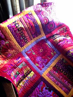 a colorful quilt sitting on top of a wooden table next to a window sill