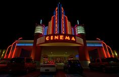 cars parked in front of a movie theater with neon lights on it's sides