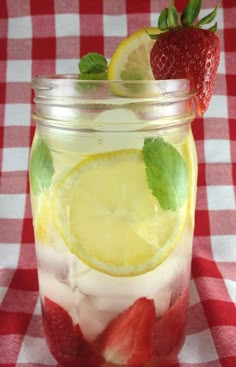 a mason jar filled with lemon, strawberries and mint on a checkered table cloth