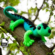 a crocheted gecko sitting on top of a tree branch with green leaves