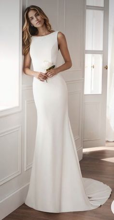 a woman in a white wedding dress standing by a window with her hands on her hips