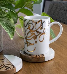 a coffee cup sitting on top of a wooden table next to a potted plant