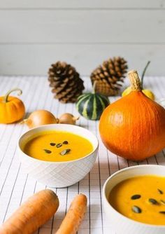 two bowls filled with carrot soup next to pumpkins and pine cones on a table