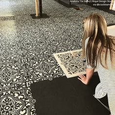 a woman is sitting on the floor and looking at an area rug that has been painted with black and white designs