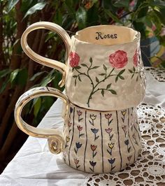 two coffee mugs sitting on top of a table next to each other with roses painted on them