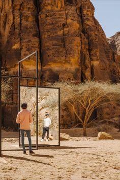 a man standing in front of a mirror on the side of a road with mountains behind him