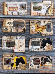 several pieces of altered paper with butterflies and moths on them sitting on a wooden surface