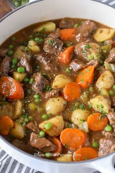 beef stew with carrots, potatoes and peas in a white pot on a striped cloth