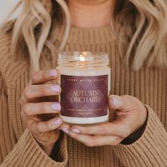 a woman holding a jar of autumn orchard candle in front of her face and hands