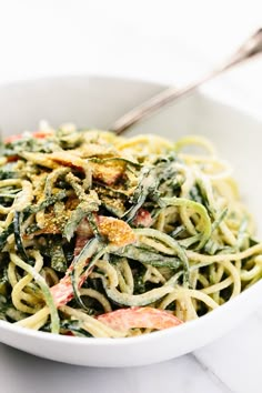 a white bowl filled with pasta and spinach on top of a marble countertop