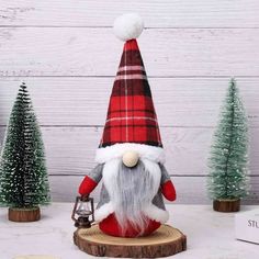 a red and white gnome statue sitting on top of a wooden stump next to christmas trees