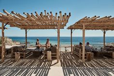 two people sitting on wooden benches near the ocean and an outdoor seating area with chairs