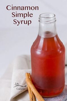 a glass bottle filled with cinnamon syrup next to two cinnamon sticks on top of a napkin