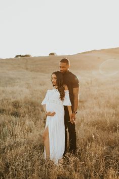 a pregnant couple standing in the middle of a field