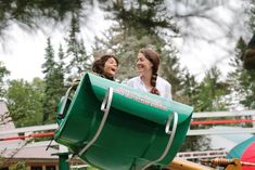 two women sitting in a large green dumpster next to each other on a playground