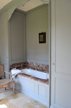 a bath tub sitting in the middle of a bathroom next to a chair and door