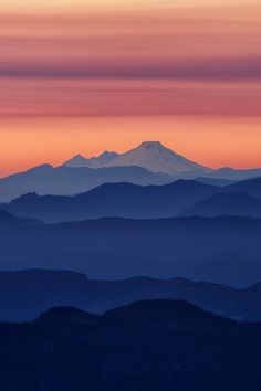 the mountains are covered in fog as the sun sets