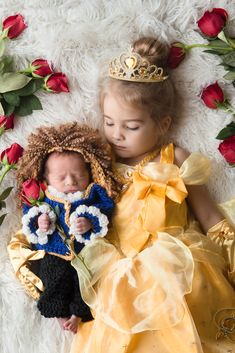 two babies dressed as princesses sleeping next to each other on a white rug with roses