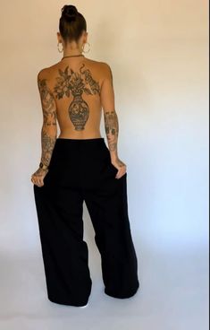 a woman with tattoos on her back standing in front of a white wall and wearing black pants