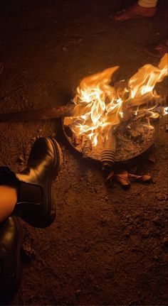 a person sitting in front of a fire with their feet on the ground next to it