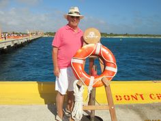 a man standing next to a life preserver near the ocean with his hat on