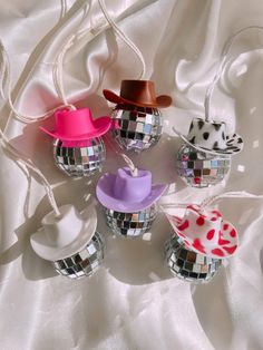 four disco balls with hats on them sitting on a white cloth covered tablecloth,