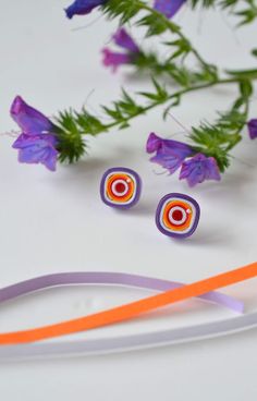 an orange and white pair of earrings next to purple flowers