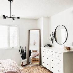 a bedroom with white walls and flooring has a large mirror on the wall above the bed